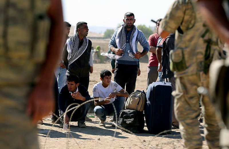 Turkish soldiers stand guard as several hundred Syrian refugees wait, at the border in Suruc, Turkey, Sunday, Sept. 21, 2014. Turkey opened its border Saturday to allow in up to 60,000 people who massed on the Turkey-Syria border, fleeing the Islamic militants’ advance on Kobani. (AP Photo/Burhan Ozbilici)