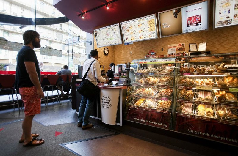 Customers wait for their orders at a Tim Hortons Inc. restaurant in Vancouver, Canada, in August. Burger King Worldwide Inc.’s plan to buy Tim Hortons Inc. and move its address to Canada is proceeding, a company spokesman said.