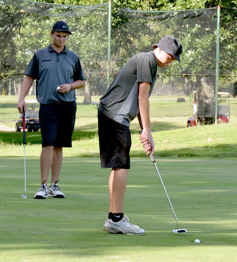 Graham Thomas/Herald-Leader Siloam Springs sophomore golfer Cody Beyer taps in a putt Monday during the match against Greenwood at Siloam Springs Country Club as senior Brandon Coale looks on.