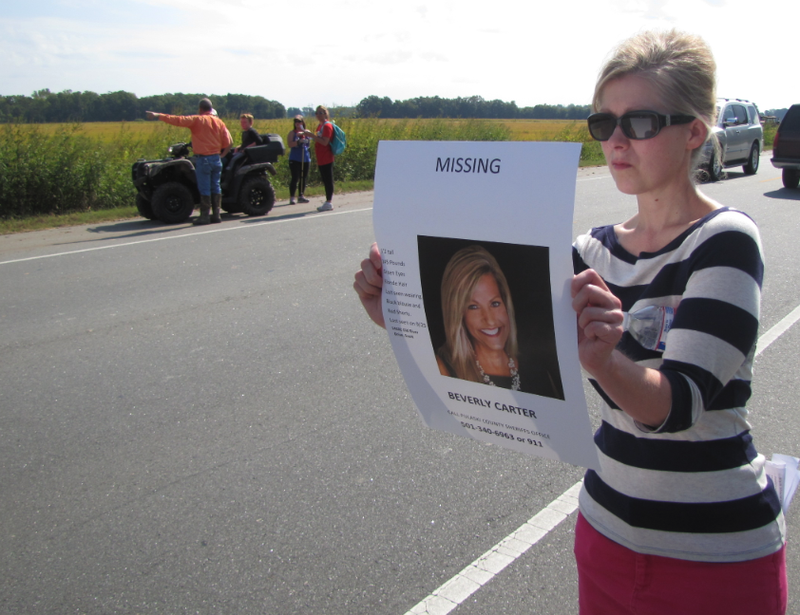 Terri Ezell holds up a sign with Beverly Carter's photo so passing motorists can see it while volunteers search along U.S. 165 in Scott. Carter disappeared after showing a home in the area Thursday night.