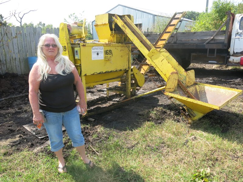 Photo by Susan Holland Barb Bates, who operates Bates Auto Sales and Bates Upholsterers on Arkansas Highway 72, west of Gravette, stands beside the walnut huller where she is now buying black walnuts. Barb began buying nuts today and will continue through Nov. 1. This is the 13th year she and her son Jodie have purchased walnuts for Hammons Products Company.