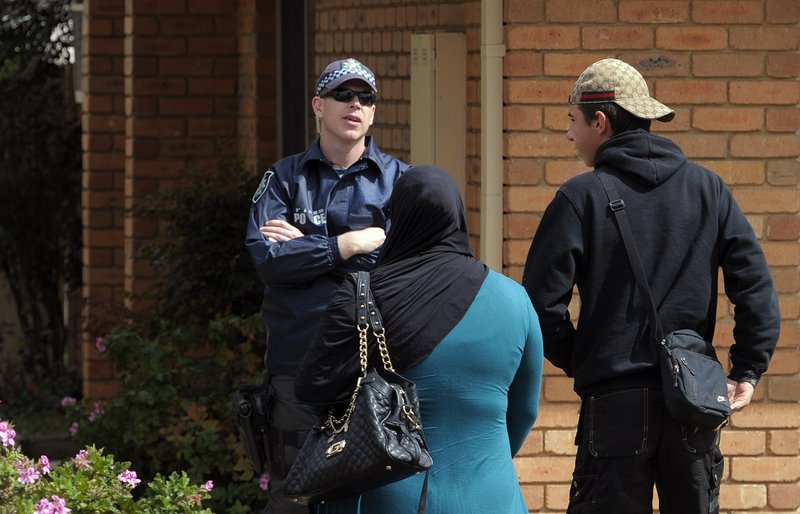 A police officer, left, speaks with two people outside of a house where a man was taken into custody during a counterterrorism raid in Seabrook in suburban Melbourne, Australia, Tuesday, Sept. 30, 2014. The man was arrested after police said he provided money to a U.S. citizen fighting alongside extremists in Syria. 
