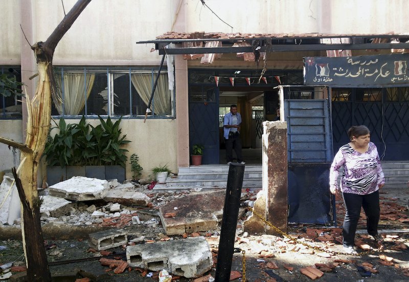 In this photo released by the Syrian official news agency SANA, Syrian citizens check the damaged school entrance in Akrama neighborhood in Homs province, Syria, on Wednesday, Oct. 1, 2014. Twin bombings near a school in central Syria killed over a dozen of people on Wednesday, as gruesome images appeared on social media networks purported to show Kurdish fighters slain at the hands of Islamic State militants during battles near Syria's border with Turkey.