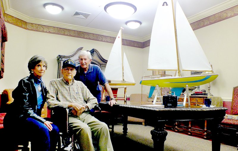 Brandon Howard/The Weekly Vista Harvey Brown, center, poses with his daughter, Shirley Kellogg and her husband, Jack, at Highlands Healthcare &amp; Rehab in front of the model boats he built. Brown began experimenting with model building when he was a youngster in Michigan.