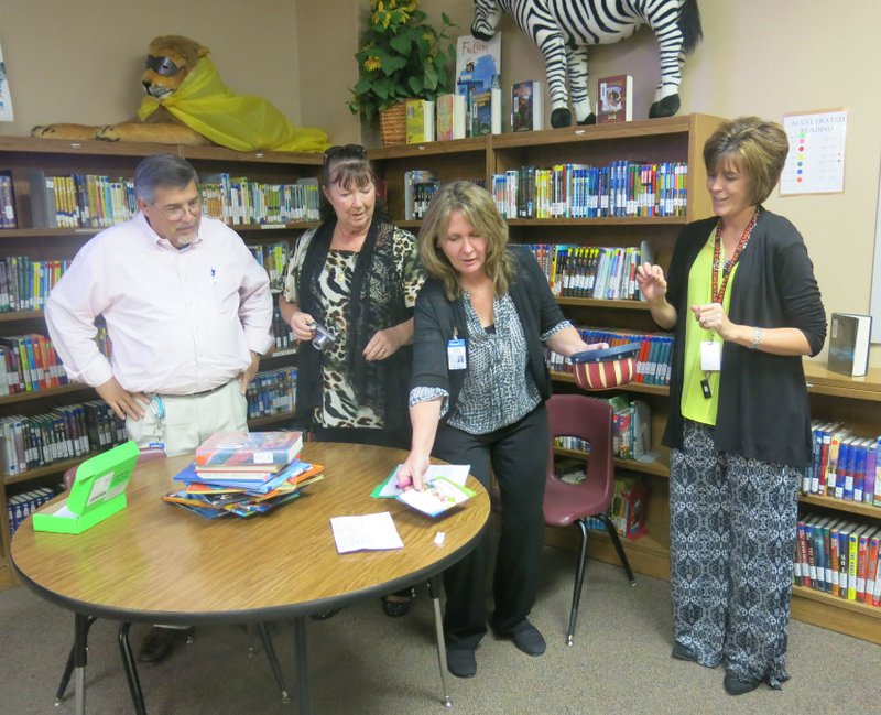 Bob Dixon, Walmart transportation manager, along with Debbie Hall and Marla King, also representing Walmart, were at last Wednesday&#8217;s staff meeting at Gravette Upper Elementary School to present 20 teachers with $50 reward cards. Bob and Debbie look on while Marla places a card on the table. Mandy Barrett, Upper Elementary principal, waits at right to draw the next name for a winning teacher. Photo by Susan Holland