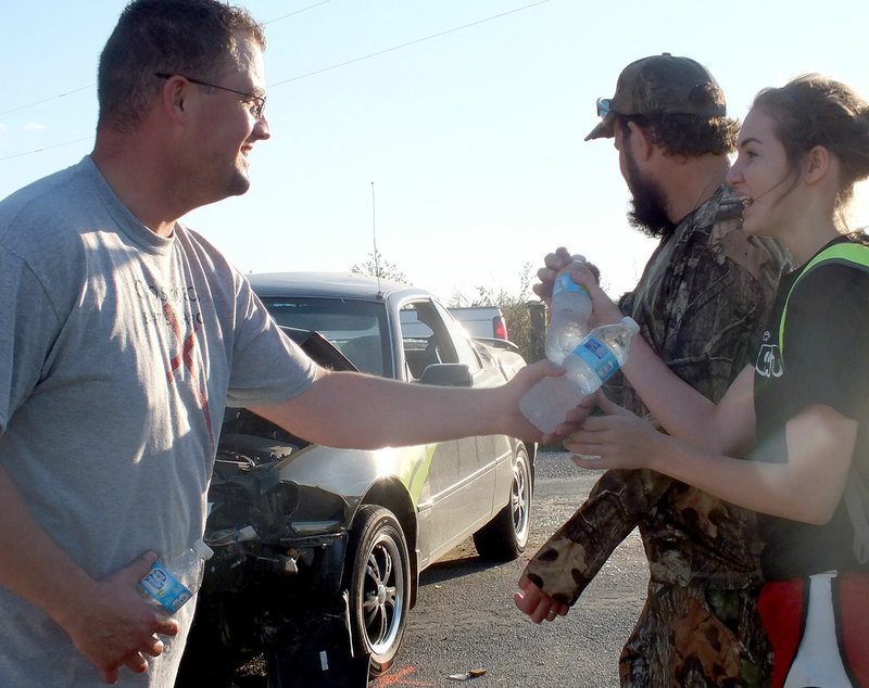 TIMES photograph by Annette Beard Bobby Shockley, left, pastor of Cross Roads Baptist Church, hands bottles of water to Rebekah and James McKeever Sunday afternoon after the McKeevers were involved in a head-on collission on Lee Town Road right in front of the church where a fall festival was being held.