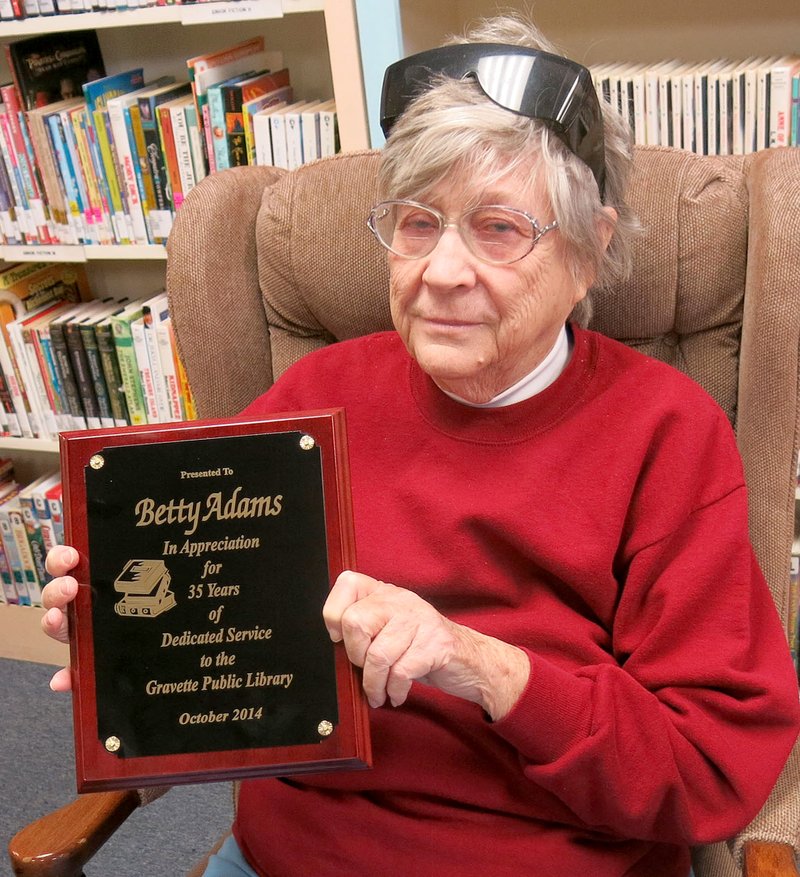 Photo by Susan Holland
Betty Adams displays the plaque she received Saturday at a party honoring her for 35 years of volunteer service to the Gravette Public Library. Betty has announced she is retiring from her volunteer duties after recent health problems. Mayor Byron Warren and library staff members were on hand to wish her well. She also received a bouquet of flowers and cake and Dr. Pepper floats were served.
