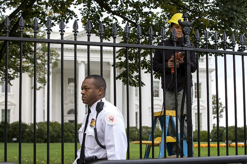 ** UPDATES THE CHARGES FILED AGAINST DOMINIC ADESANYA ** A Secret Service police officer walks outside the White House in Washington, Thursday, Oct. 23, 2014, as a maintenance worker performs fence repairs as part of a previous fence restoration project. Dominic Adesanya, the 23-year-old Maryland man who climbed over the White House fence was ordered held without bond in an appearance Thursday before a federal magistrate judge. He has been charged with unlawfully entering the restricted grounds of the White House and harming two police dogs. (AP Photo/Evan Vucci)