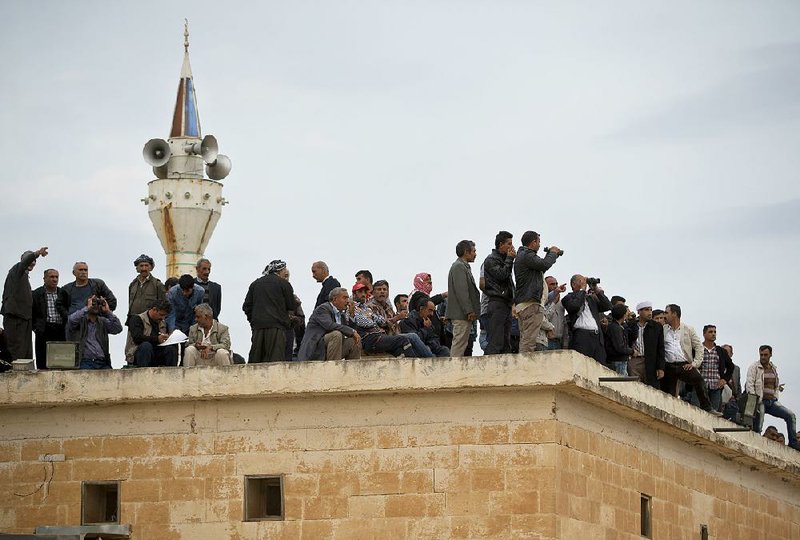 People stand on the roof of the village mosque in Caykara, on the Turkey Syria watching fighting across the border in the Syrian town of Kobani, Monday, Oct. 27, 2014. Kobani, also known as Ayn Arab, and its surrounding areas, has been under assault by extremists of the Islamic State group since mid-September and is being defended by Kurdish fighters. (AP Photo/Vadim Ghirda)
