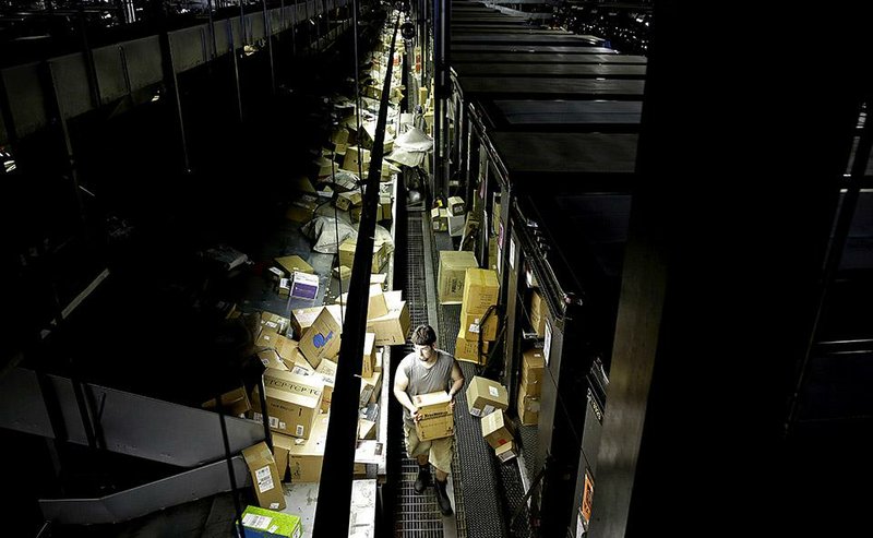 A worker carries a box while loading trucks before deliveries at the United Parcel Service sorting facility in Roswell, Ga., in June.