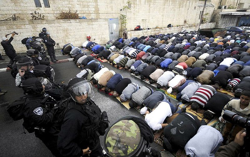 Israeli border police block a road as Palestinians pray in Jerusalem on Friday, Oct. 31, 2014. Israel reopened a contested Jerusalem holy site, known to Jews as the Temple Mount and Muslims as the Noble Sanctuary, on Friday and deployed more than 1,000 security personnel following clashes the previous day between Palestinians and Israeli riot police that had ratcheted up already heightened tensions in the city. (AP Photo/Mahmoud Illean)