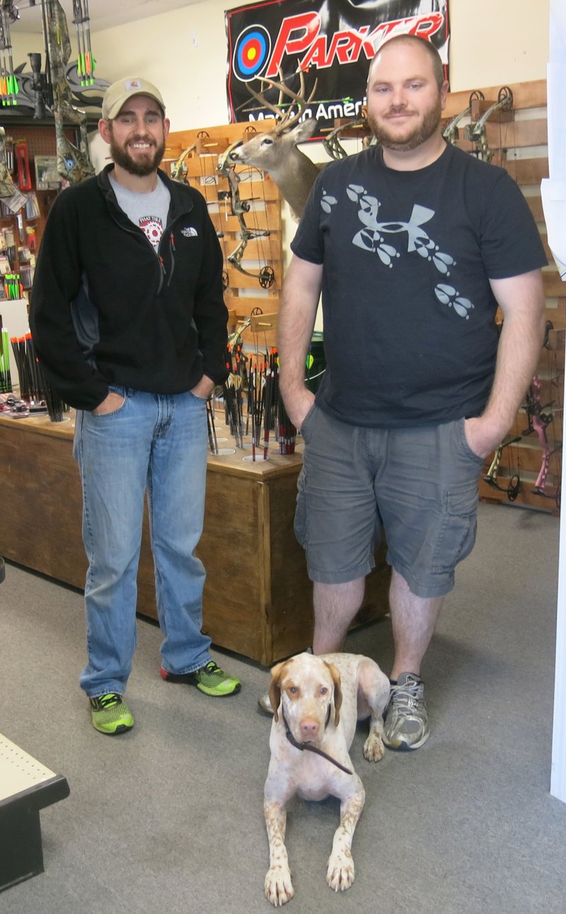 Dustin James and Jake Knoedel operate Knoedel&#8217;s Outdoor Tech in Hiwasse. They are shown here in the archery department of the business with the store mascot, Tank. The popular sporting goods business stocks a wide array of gear for archery enthusiasts, hunters and fishermen. Photo by Susan Holland
