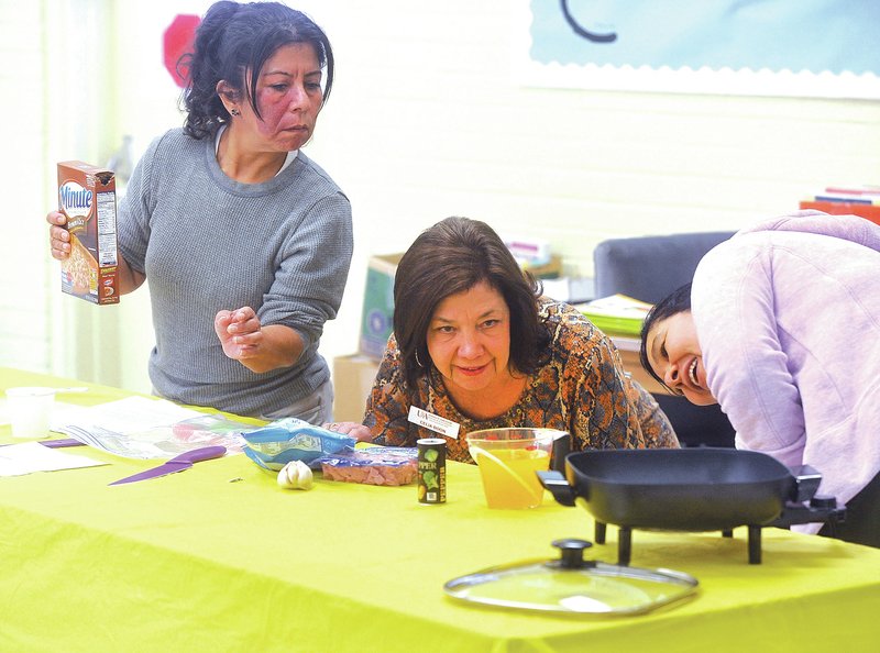 Staff Photo Michael Woods &#8226; @NWAMICHAELW Celia Boon, center, works Monday with her students Regina Sullivan, left, and Anna Henriquez as they measure out the ingredients for their lunch dish morning during a nutrition and cooking class at the Fayetteville Adult Education Center in Fayetteville. The Fayetteville Adult Education Center has partnered with the University of Arkansas Cooperative Extension to offer a nutrition and cooking class to students, many of whom are ESL students.