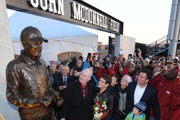 John McDonnell, former University of Arkansas cross country and track and field coach, center, and his wife, Ellen, smile as a cover is removed from a statue in his honor during a ceremony Friday, Nov. 14, 2014, at John McDonnell Field on the university campus in Fayetteville. A plaza honoring past athletes and championships was also dedicated during the ceremony.