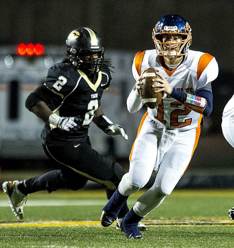 Rogers Heritage quarterback Jake Qualls (12) looks downfield to pass while Little Rock Central’s Malcom Williams gives chase during Friday night’s Class 7A playoff game in Little Rock.