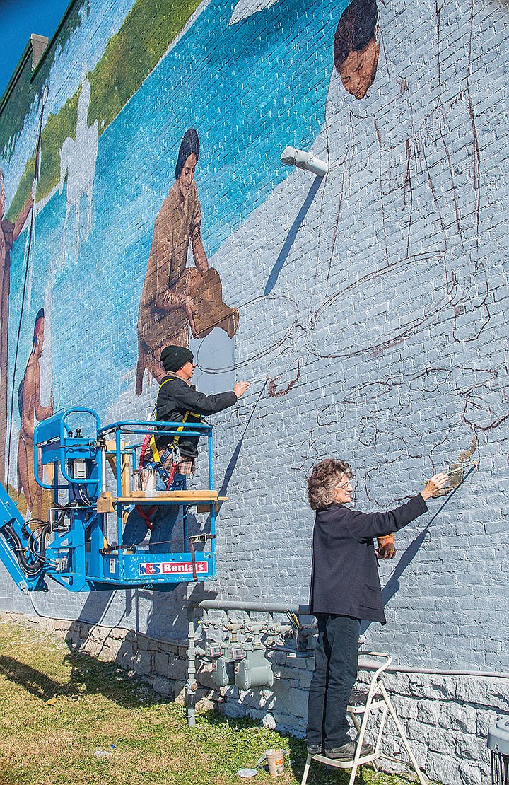 Mark Davey, left, uses a cherry picker to attain a high position as Dianne Roberts works near ground level on a mural that will depict the history of the Saline County area on this formerly blank wall of the Bell Building in downtown Benton.