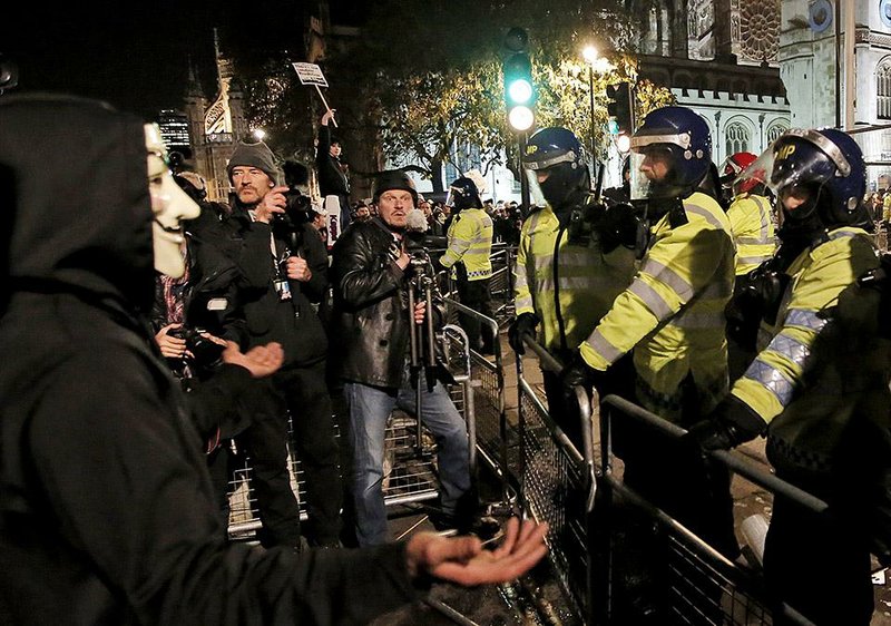 In this photo taken Wednesday, Nov. 7, 2014, freelance video journalist James Parkinson, center wearing a helmet and holding his camera on a tripod, films scuffles between British police officers, right, and anti-austerity demonstrators during a rally in central London. Parkinson, a 44-year-old freelancer who has covered hundreds of protests - some of them for The Associated Press - is among six British journalists who are suing London’s Metropolitan Police and Britain’s Home Office over police surveillance of journalists’ movements. Parkinson, three photographers, an investigative journalist and a newspaper reporter are filing the lawsuit after obtaining their surveillance records. (AP Photo/Lefteris Pitarakis)