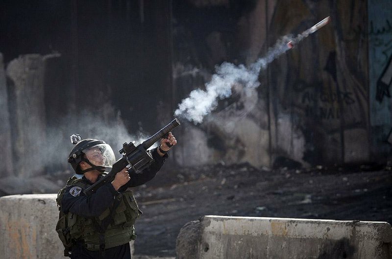 An Israeli policeman fires tear gas to disperse stone-throwing Palestinian protesters Friday at the Qalandya checkpoint near the West Bank city of Ramallah.