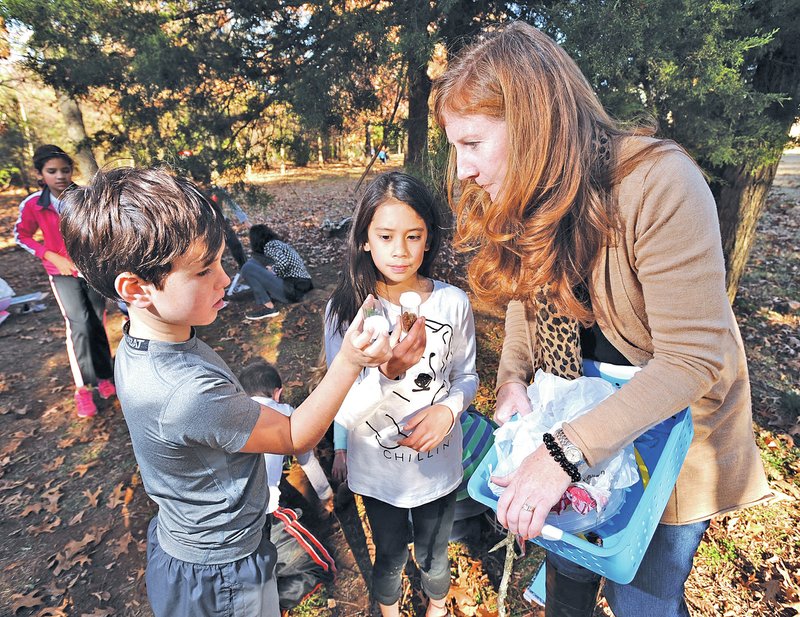STAFF PHOTO ANDY SHUPE Rebecca Wilbern, right, a fourth-grade teacher at Vandergriff Elementary School in Fayetteville, takes a look at specimens Thursdsay collected by Greyson Garrett, 10, left, and Ezra Andersen, 9, as her class spends time in search of specimens behind the school.