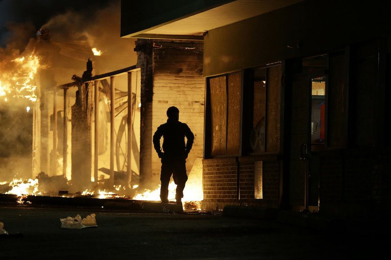 A man watches as stores burn Tuesday, Nov. 25, 2014, in Ferguson, Mo. A grand jury has decided not to indict Ferguson police officer Darren Wilson in the death of Michael Brown, the unarmed, black 18-year-old whose fatal shooting sparked sometimes violent protests.