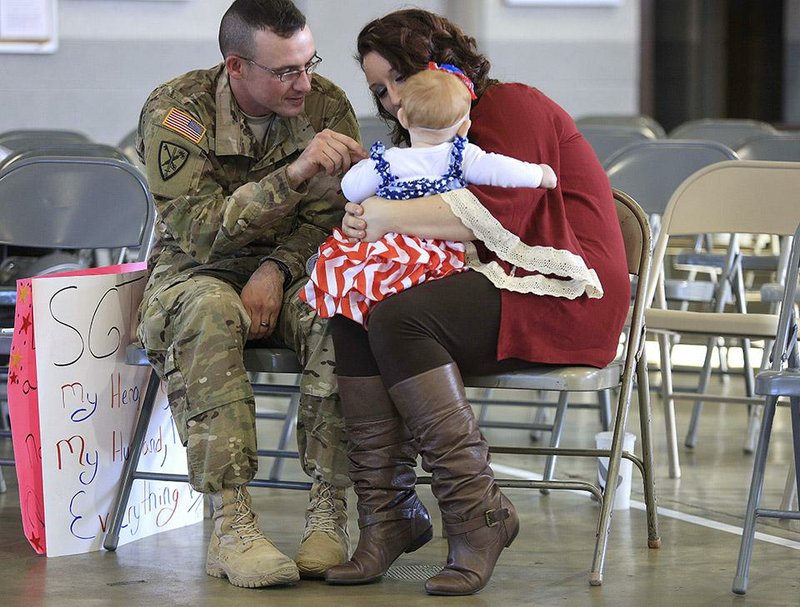 Sgt. Rick DeSalvo of Fort Smith plays with his 7-month-old daughter, Izzie, as he sits with his wife, Tati, after a welcome-home ceremony Wednesday at Fisher Armory in North Little Rock for 111 soldiers in the 216th Military Police Company.