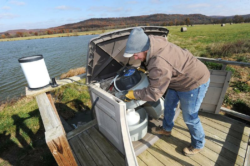 Lawrence Berry, a crop, soil and environmental sciences program technician at the University of Arkansas, makes adjustments to equipment at a collection station Tuesday at Jeff Marley’s farm near Elkins.
