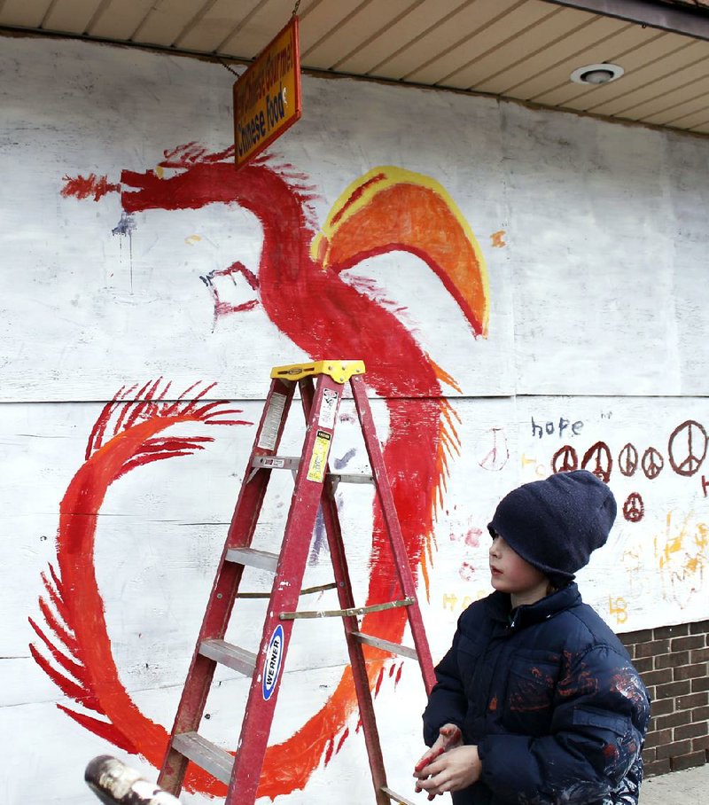 Several children aided by their parents put the finishing touches on a dragon painted on plywood Thursday in downtown Ferguson, Mo. The plywood had been placed on some buildings in Ferguson to protect them from vandals.