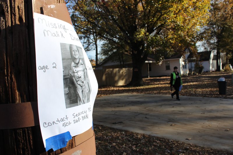 A volunteer searcher walks by a missing poster on Nov. 25 while looking for missing 2-year-old Malik Drummond.