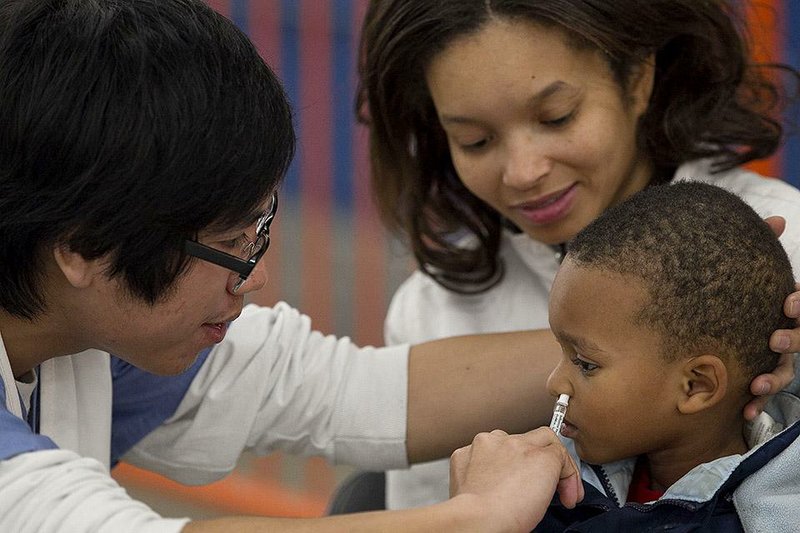 Daniel Estrella (left), a registered nurse, gives 2-year-old Kenrick Boykins a dose of flu vaccine through a nasal application Thursday during an Arkansas Health Department’s free flu-vaccinations clinic at the State Fairgrounds in Little Rock. Kendrick was accompanied by his mother, Amanda Jones. 