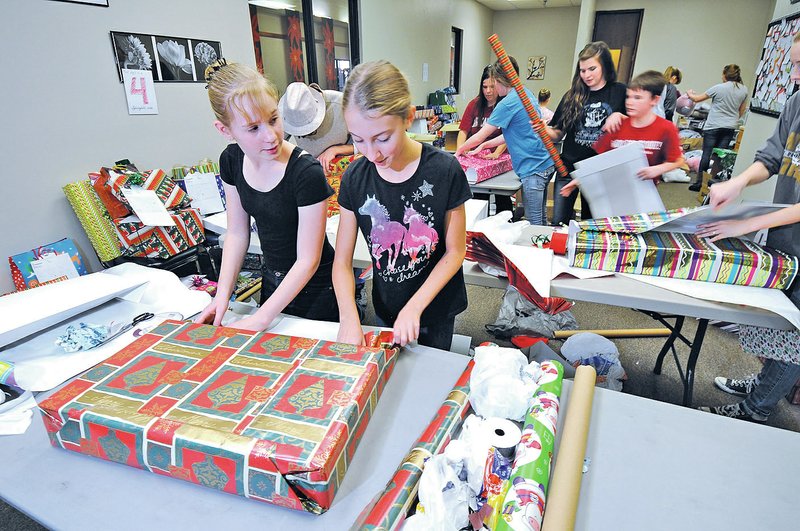  STAFF PHOTO J.T. Wampler Volunteers Anna Connolley, left, of Garfield and Lindi Blevins of Lowell wrap gifts for seniors through &#8220;Be a Santa to a Senior&#8221; Home Instead Senior Care on Monday at the Frisco Mall in Rogers. The annual holiday tradition is in its 11th year.