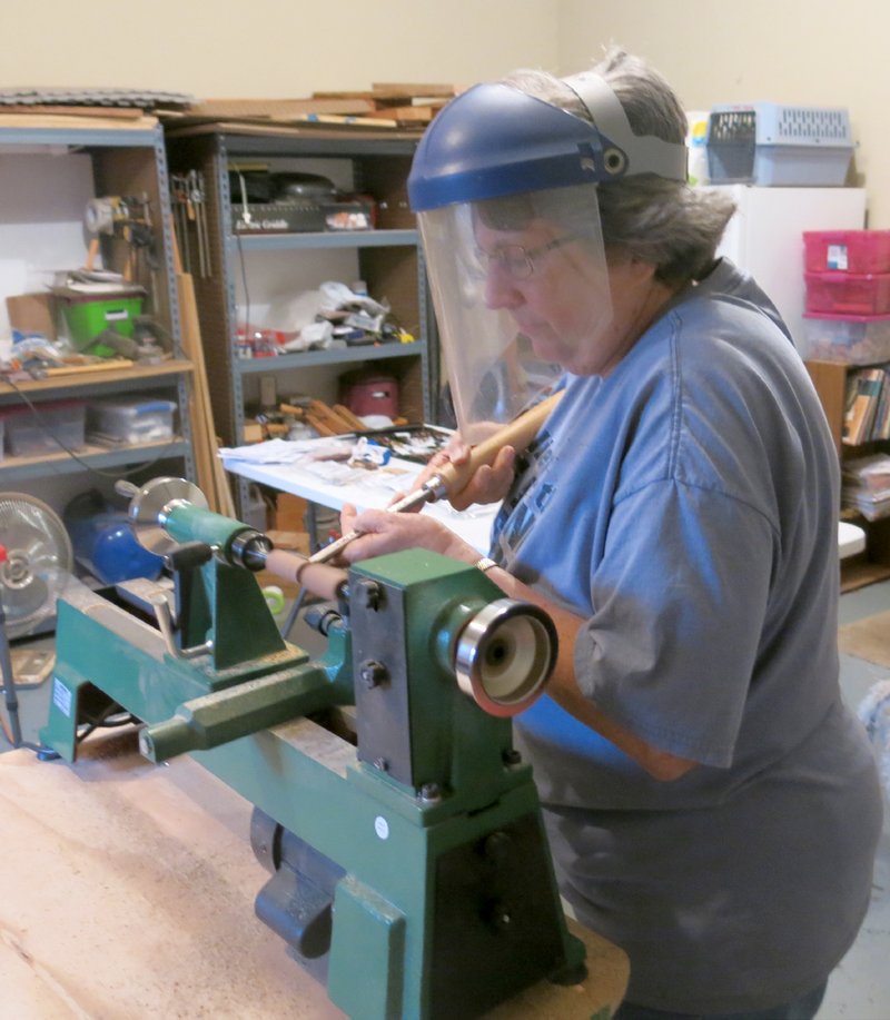 Photo by Susan Holland Gayle Williams wears a protective face shield when working at the lathe in her garage workshop. Here she is carving out the body of a pen which will then be sanded, polished and waxed to create a beautiful work of art. The lovely pens make excellent gifts for family members and friends, or you can just purchase one when you want a special treat for yourself.