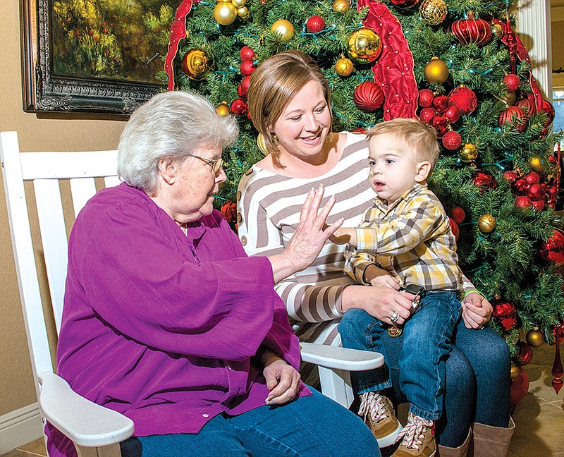 Mary Randolf, left, receives a high-five from Dexter McDade, 2, as he sits with his mother, Alexis McDade, while they get ready for the Rocking Around the Christmas Tree event for Dexter at Mount Carmel Community, an assisted- and independent-living facility in Benton. The event will raise money to help with medical expenses for Dexter, who needs a kidney transplant.