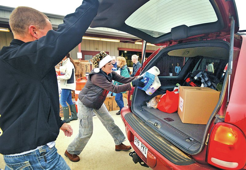 STAFF PHOTO BEN GOFF &#8226; @NWABenGoff Sarah Semrow tosses paper towels and tissues into a vehicle Friday as volunteers fill vehicles with donated food and household supplies during the Sharing &amp; Caring Benton County holiday gift distribution day at the Benton County Fairgrounds in Bentonville.