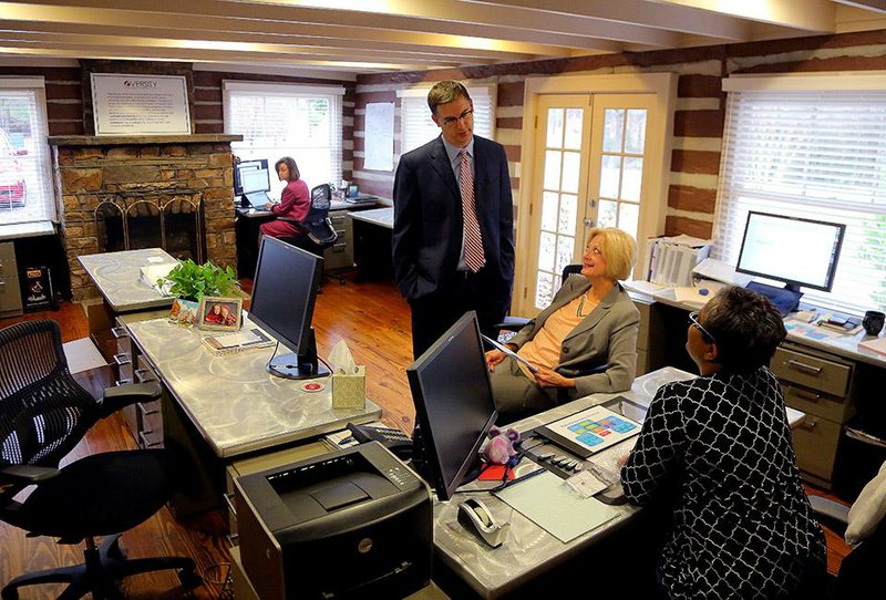 Michael Moore, the University of Arkansas System’s vice president for academic affairs, talks Friday with Kim Bradford and Harriet Watkins inside the eVersity offices in an old log cabin on the UA System campus in Cammack Village. 