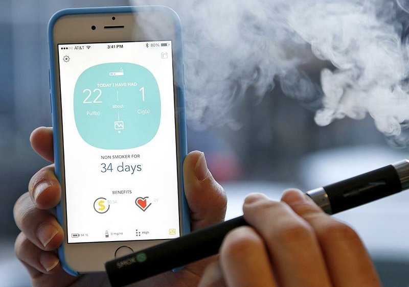 In this Wednesday, Nov. 19, 2014 photo, a smoker poses for photos while taking a puff on a Smokio, an electronic cigarette or vaporizer that connects to an iPhone and other smartphones via Bluetooth to track puffs, tally the cost-savings and possible health benefits from switching from regular cigarettes, in Richmond, Va. E-cigarette technology is developing rapidly and federal officials say the technology race could make creating standards for the devices, which heat a liquid to create vapor rather than burning tobacco, more difficult in the future. (AP Photo/Steve Helber)