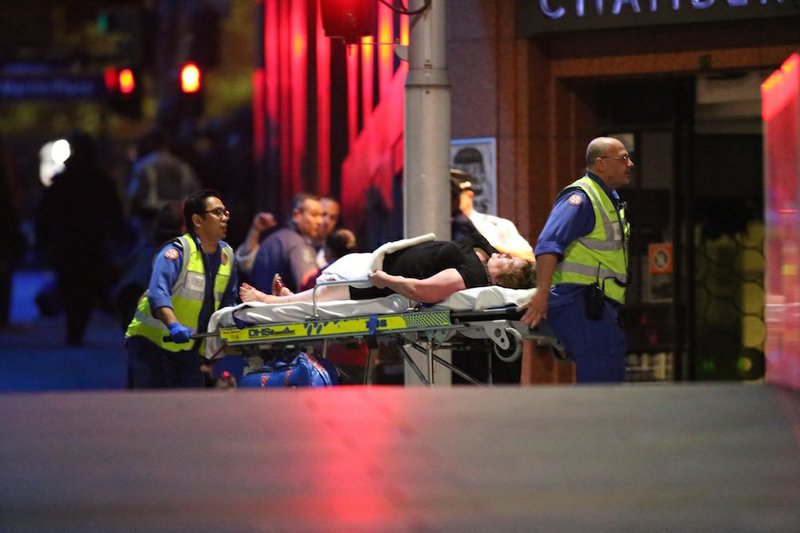 A injured hostage is wheeled to an ambulance after shots were fired during a cafe siege at Martin Place in the central business district of Sydney, Australia, on Tuesday, Dec. 16, 2014. New South Wales state police would not say what was happening inside the cafe or whether hostages were being held. But television footage shot through the cafe's windows showed several people with their arms in the air.