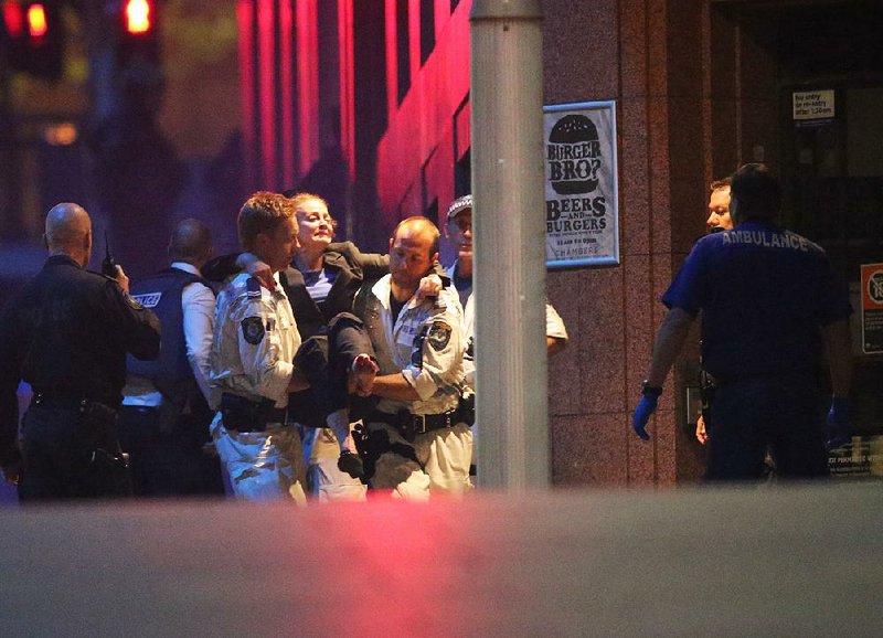 A injured hostage is carried to an ambulance after shots were fired during  a cafe  siege at Martin Place in the central business district of Sydney, Australia, Tuesday, Dec. 16, 2014. New South Wales state police would not say what was happening inside the cafe or whether hostages were being held. But television footage shot through the cafe's windows showed several people with their arms in the air.(AP Photo/Rob Griffith)