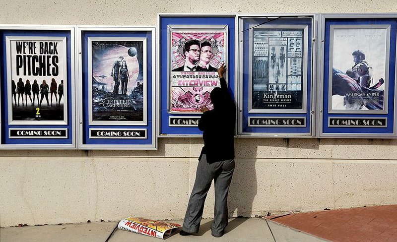 An employee removes a poster for The Interview at a Carmike Cinemas theater Wednesday in Atlanta. The Carmike chain was the first to cancel showings of the comedy set for a Christmas Day release.