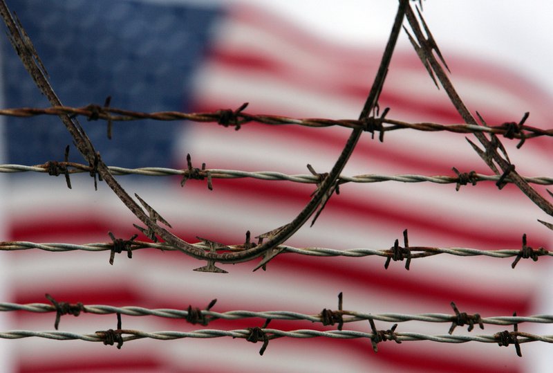 In this Oct. 10, 2007 file photo, reviewed by the U.S. Military, an American flag flies behind the barbed and razor-wire at the Camp Delta detention facility, at Guantanamo Bay U.S. Naval Base, Cuba. The Pentagon said Saturday that four Afghans from the Guantanamo Bay detention center have been returned to their home country in what U.S. officials are citing as a sign of their confidence in new Afghan President Ashraf Ghani. 