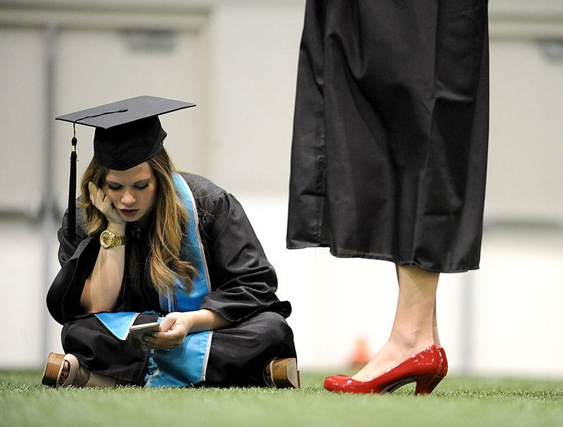 Hannah Sellers of Bryant looks at her cellphone while waiting with other graduates before the start of the University of Arkansas fall commencement exercises Saturday at Barnhill Arena in Fayetteville. 