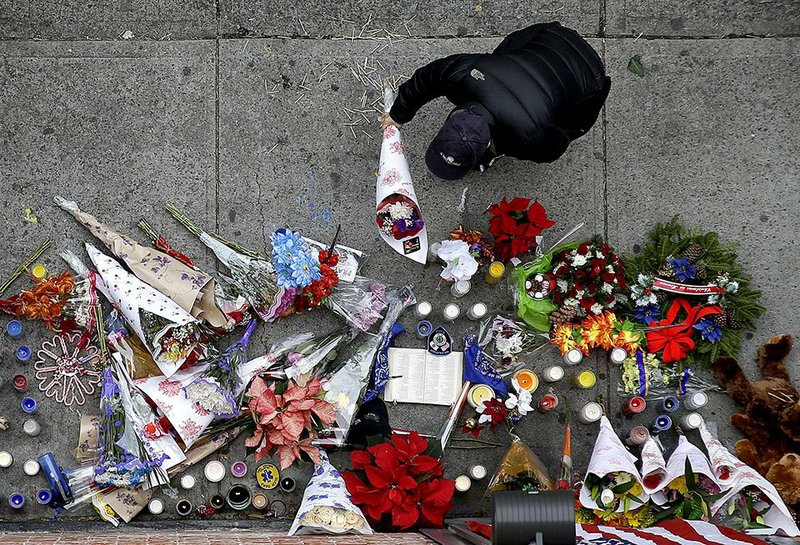 A man leaves flowers at an impromptu memorial near the site where two police officers were killed the day before in the Brooklyn borough of New York, Sunday, Dec. 21, 2014. Police say Ismaaiyl Brinsley ambushed officers Rafael Ramos and Wenjian Liu in their patrol car in broad daylight Saturday, fatally shooting them before killing himself inside a subway station. (AP Photo/Seth Wenig)