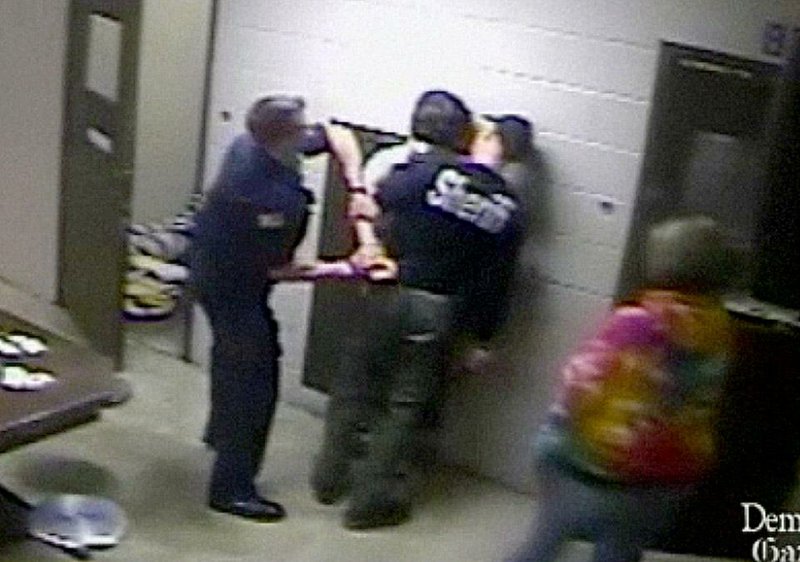 Danville Police officer Timothy Spears, left, starts to thrust the arm of juvenile D.B. up, near his head, breaking it in two places as Yell County Sheriff's Deputy Michael Spears, right, holds D.B. against the wall at the Yell County Juvenile Detention Center on March 22, 2014, in this video frame grab.