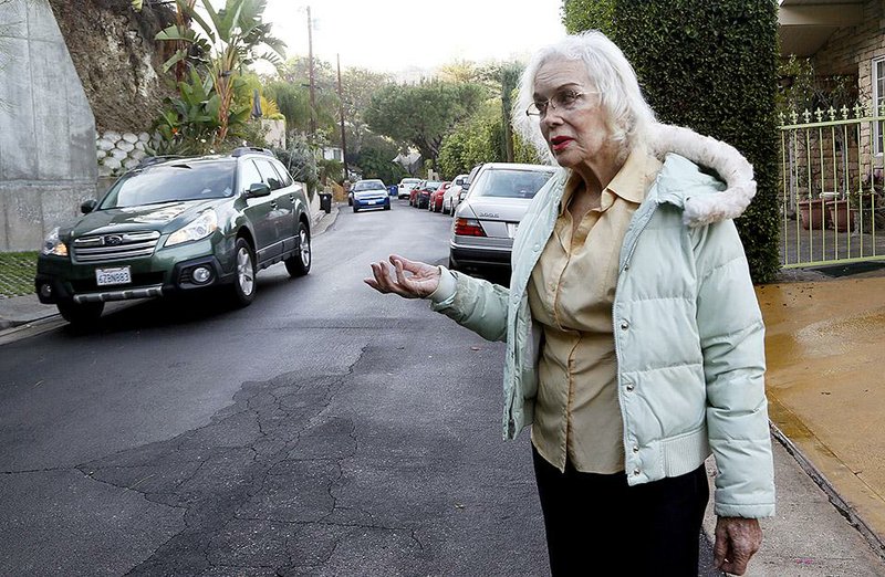 In t Thursday, Dec. 4, 2014 photo resident Paula Hamilton stands on a street outside her house in the Sherman Oaks section of Los Angeles. "The traffic is unbearable now. You can't even walk your dog," said Hamilton, who lives on a once quiet little street. When the people whose houses hug the narrow warren of streets paralleling the busiest urban freeway in America began to see bumper-to-bumper traffic rushing by their homes a year or so ago they were baffled. When word spread that the explosively popular new smartphone app Waze was sending many of those cars through their neighborhood in a quest to shave five minutes off a daily rush-hour commute, they were angry and ready to fight back. (AP Photo/Nick Ut)