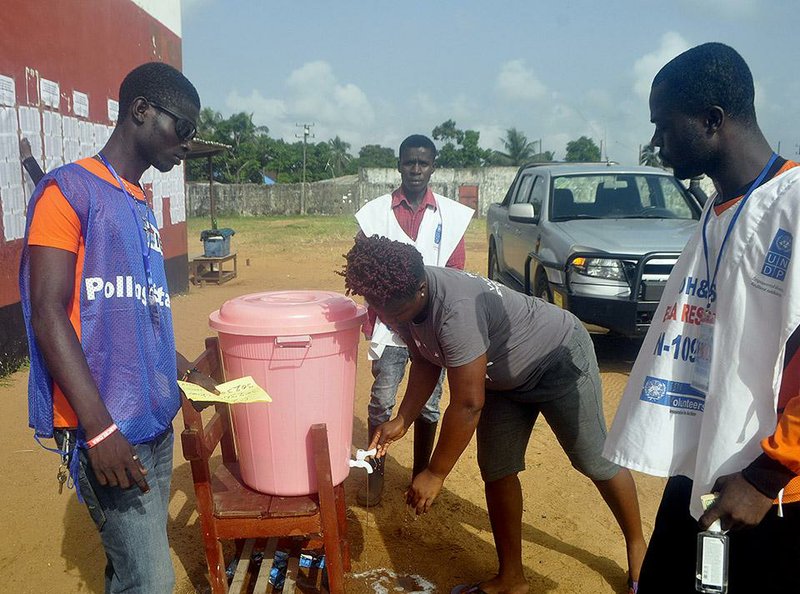 Liberian election workers watch Saturday in Monrovia as a woman washes her hands before voting in the country’s twice-delayed Senate election.