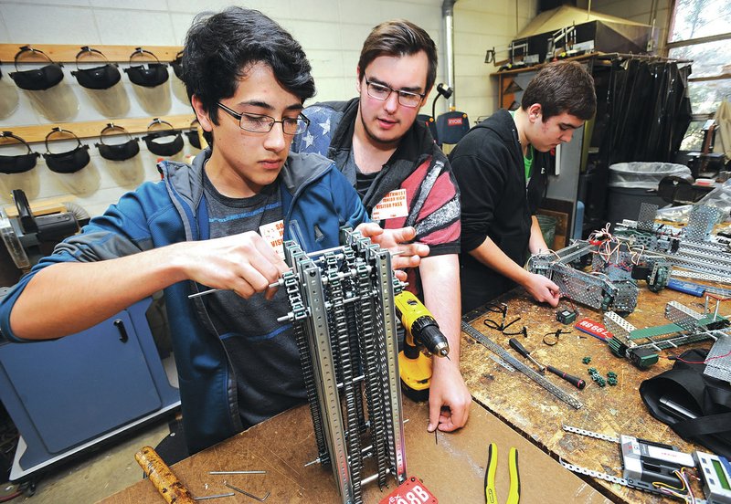 STAFF PHOTO ANDY SHUPE Juan Zuniga, 15, left, and Brayden Rose, 16, replace parts on a robot component as Noah Wehn, 16, right, assembles a part.