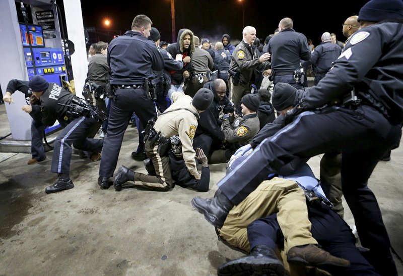 Police try to control a crowd Wednesday, Dec. 24, 2014, on the lot of a gas station following a shooting Tuesday in Berkeley, Mo. St. Louis County police say a man who pulled a gun and pointed it at an officer has been killed.