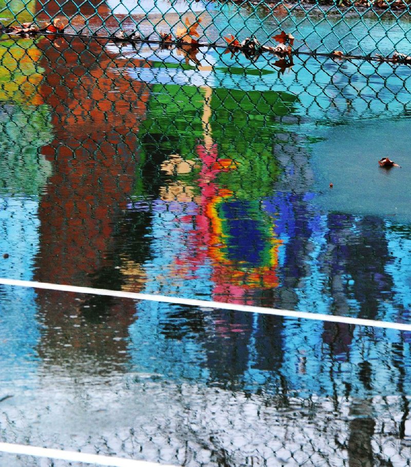 The Walker Park Historical Mural is reflected in the rain puddles on the tennis courts at Walker Park in Fayetteville on Wednesday. The rain is expected to clear out by Christmas morning with highs in the 50s for Northwest Arkansas.