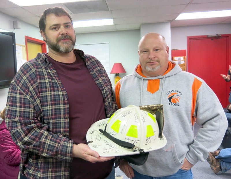 Photo by Susan Holland Assistant fire chief Chuck Skaggs, right, presented chief David Smith a fire helmet signed by his fellow firefighters at a retirement party held at the fire station last Tuesday night. Smith was being honored for his 20 years of service to the Gravette fire department, 11 of which were as chief. Smith is retiring at the end of the year.