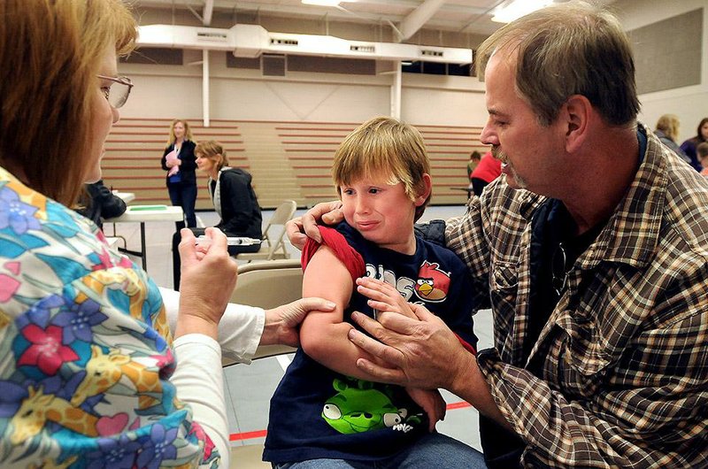 Rocky Brace (right) comforts his grandson, Lane Brace, 6, as nurse Caroline Wilson with the Arkansas Department of Health administers a flu vaccination during the annual flu vaccination clinic at the Rogers Activity Center in this Oct. 25, 2013, file photo. Two Arkansans have died from the virus so far this flu season. 