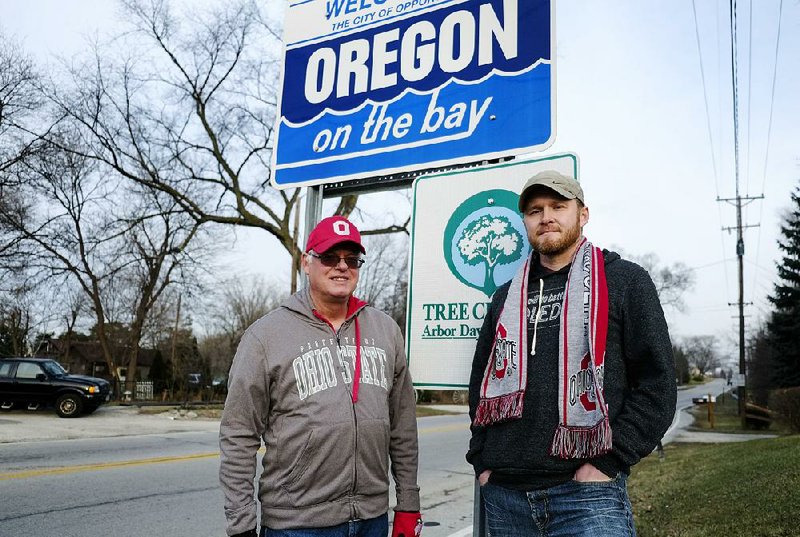 In this Jan. 2,  2015 photo, Dick Squibb and his son Matt, right, stand at the Oregon, Ohio, city limits sign. The Ohio city of Oregon isn't going to be known as "Buckeye Town" or any other title despite a petition calling for a temporary name change to show allegiance to the Ohio State Buckeyes as they face the Oregon Ducks in college football's championship game next week. The mayor of the Toledo suburb, instead, said he intends to issue a proclamation declaring it "Ohio State Buckeye week" in the city of Oregon. Matt Squibb, one of the petition organizers, said he didn't want anyone confused who the city would be cheering for during the title game. (AP Photo/The Blade, Andy Morrison)   MANDATORY CREDIT; MAGS OUT; NO SALES; TV OUT; HUFFINGTON POST OUT; SENTINEL-TRIBUNE OUT; MONROE EVENING NEWS OUT; TOLEDO FREE PRESS OUT